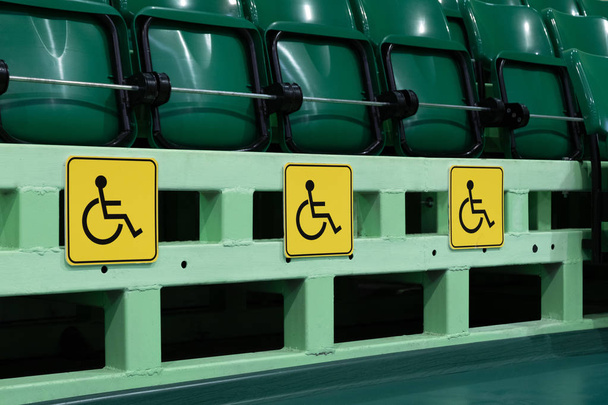 Plätze für Behinderte in der Aula. grüne Sitze in einem Stadion oder in einem Sportkomplex. Konzept zum Schutz der Rechte von Menschen mit einer Verletzung des Muskel-Skelett-Systems. gelbes Symbol. - Foto, Bild
