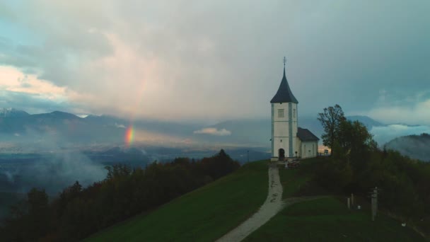 Luftaufnahme der Kirche des Heiligen Tomas im oberen Savatal in Slowenien. Berglandschaft mit Regenbogen - Filmmaterial, Video