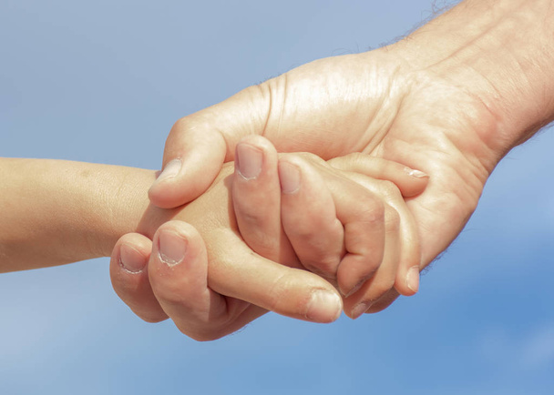 Απλώνουν το χέρι με χέρι. Χέρια ενός πατέρα στην κόρη του με το μπλε του ουρανού.  - Φωτογραφία, εικόνα