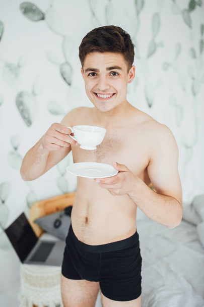 Young handsome man with bare torso drinking coffee in room in morning - Foto, Imagem