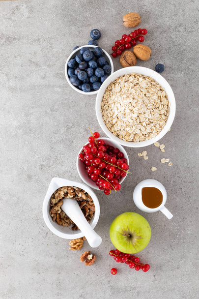 Cooking oatmeal with fresh berries, blueberry, red currant, walnuts and honey. Healthy vegetarian breakfast food concept, top view, flat lay - Foto, Bild