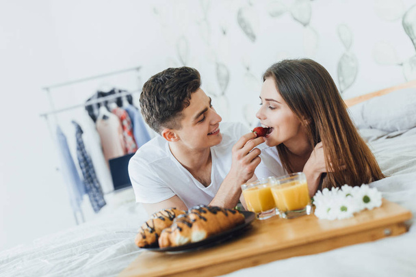 young couple eating breakfast in bed in morning, focus on foreground - Фото, изображение