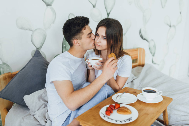 Young cute couple drinking coffee in bed at home, selective focus - Фото, изображение