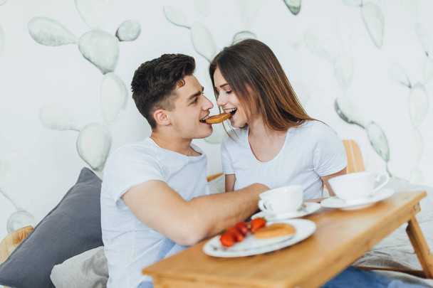 Young couple eating biscuits in form of heart, coffee in bed - Φωτογραφία, εικόνα