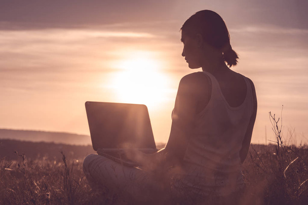 Silhouette eines Mädchens mit Laptop auf Sonnenuntergang oder Sonnenaufgang Hintergrund - Foto, Bild