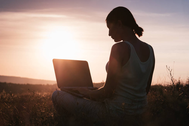 silhouet van een meisje met laptop op zonsondergang of zonsopgang achtergrond - Foto, afbeelding
