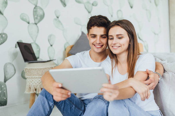 Joven bonita pareja en casa sentada en el suelo y mirando la tableta digital
 - Foto, imagen