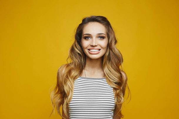 Beautiful and fashionable blonde model girl with a charming smile in white striped dress has a fun and posing at the yellow background, isolated - Zdjęcie, obraz