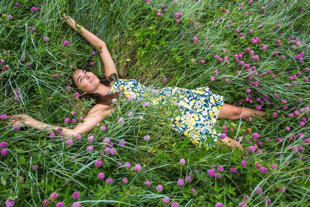 summer walk on a green ravine, a young slim pretty girl with long brown hair in a yellow dress sundress, enjoys life on the field with summer flowers - Foto, imagen