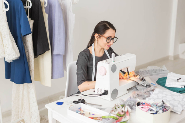 Dressmaker, sastre, obras y concepto de costurera - Retrato de alta vista angular de diseñador de moda sonriente en gafas usando máquina de coser
 - Foto, Imagen