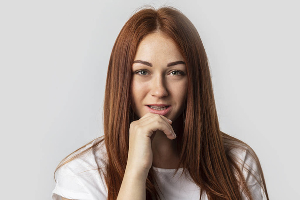 Close-up young red-haired woman isolated on gray background. She looks into the camera and flirts - Fotoğraf, Görsel