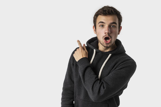 Amazed caucasian young man pointing backwards with shocked face and looking into the camera. Isolated on white background. Advertisement concept. - Фото, изображение