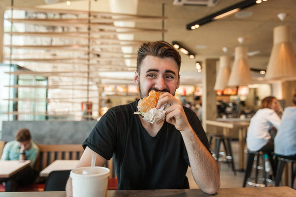 A man eats a burger at dinner in a cafe. - Foto, afbeelding