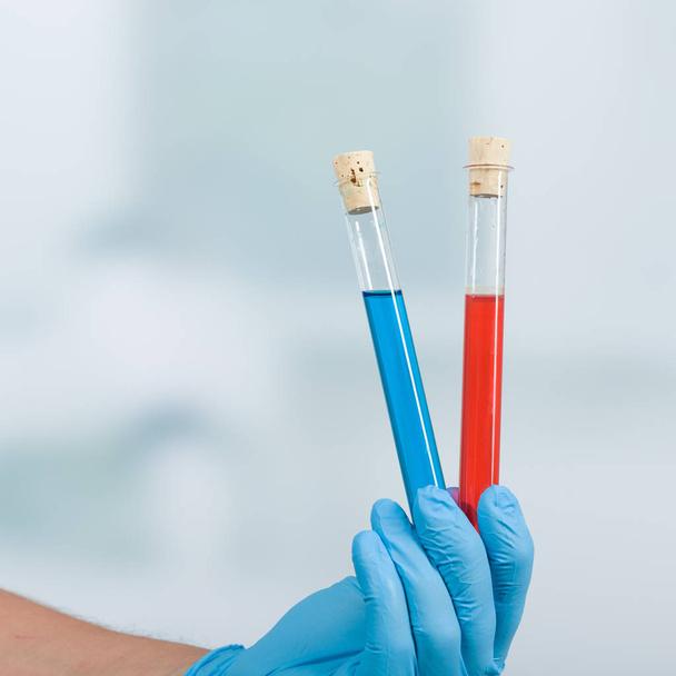 mano in guanti tiene una provetta con liquido blu e rosso davanti a uno sfondo di laboratorio
 - Foto, immagini
