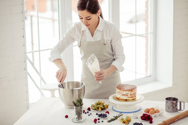 young attractive chef putting cream in the pastry bag - Photo, image