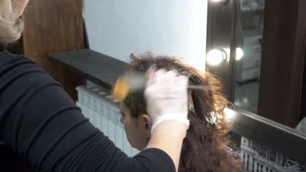 Eine Friseurin bemalt einem Mädchen in einem Friseursalon die Haare und streicht sich mit einem Pinsel Farbe auf den Kopf. Haarpflege. Nahaufnahme. 4k. 25 fps. - Filmmaterial, Video