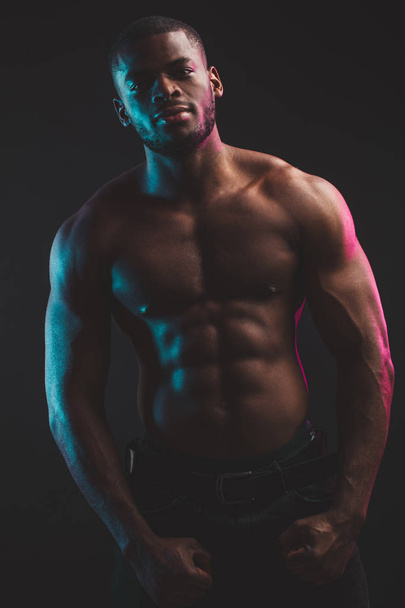 African male athlete with naked torso posing against dark wall. Low key photo. - Foto, imagen