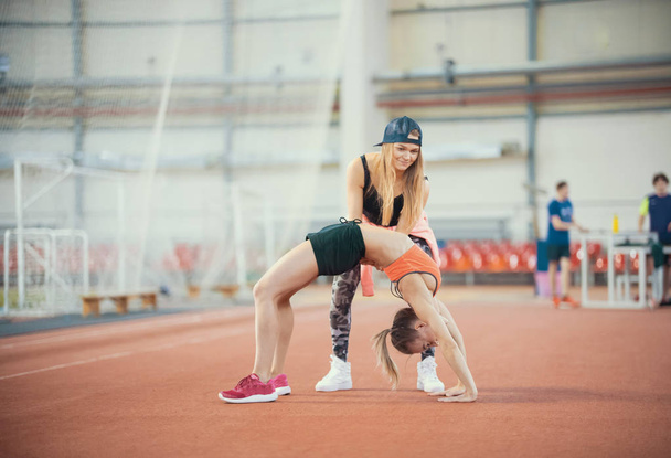 zwei junge Frauen mit blonden Haaren beim gemeinsamen Turnen und Atemholen in der Sporthalle - Foto, Bild