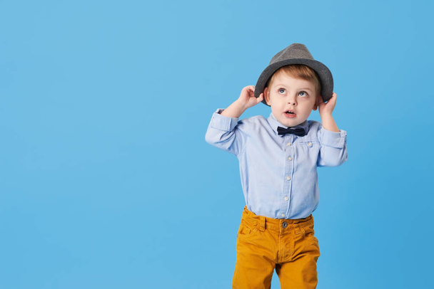 Portrait of happy joyful  little boy isolated on blue background. Toddler child in hat and fashionable suit smiling and have a fun  - Fotoğraf, Görsel