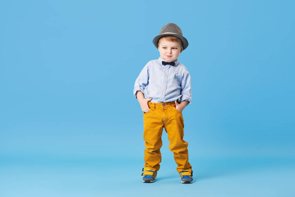 Portrait of happy joyful  little boy isolated on blue background. Toddler child in hat and fashionable suit smiling and have a fun  - Zdjęcie, obraz