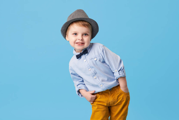 Portrait of happy joyful  little boy isolated on blue background. Toddler child in hat and fashionable suit smiling and have a fun  - Φωτογραφία, εικόνα