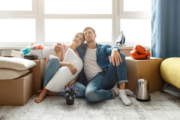 Young family couple bought or rented their first small apartment. Two people sit on floor and look up. They dream. Guy hug young woman. They smile. - Foto, Imagen