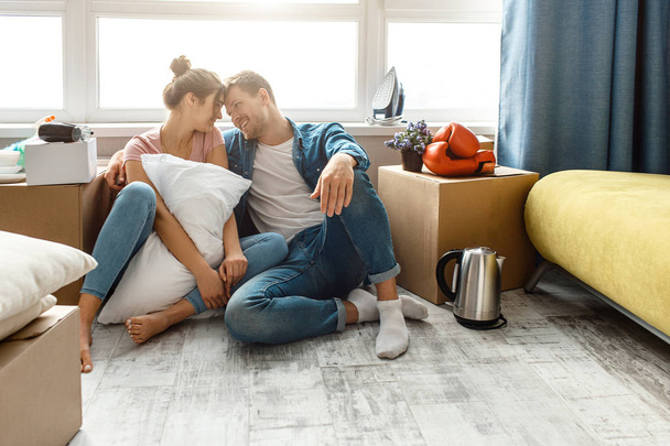 Young family couple bought or rented their first small apartment. They sit on floor very close and enjoy each other company. Moving unpacking. Lovely cheerful couple. - Fotó, kép
