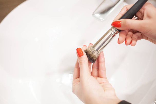 Макіяж пензлем. Жінка миє брудний пензлик для макіяжу з милом і піною в раковині
 - Фото, зображення