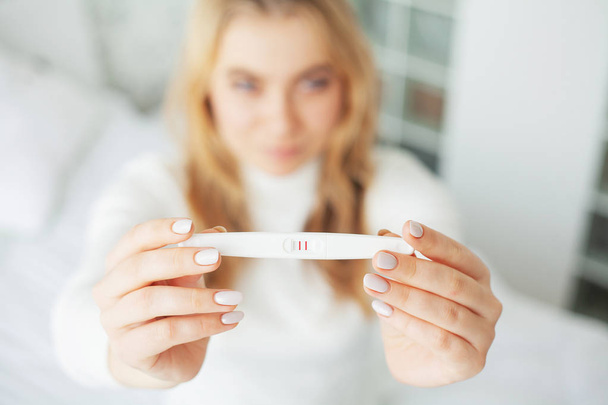 Schwangerschaftstest. Besorgte traurige Frau schaut nach Ergebnis auf Schwangerschaftstest - Foto, Bild