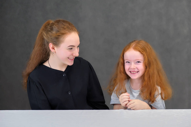 Concept portrait de deux jolies filles mignonnes soeurs aux cheveux roux sur un fond gris souriant et parlant
. - Photo, image
