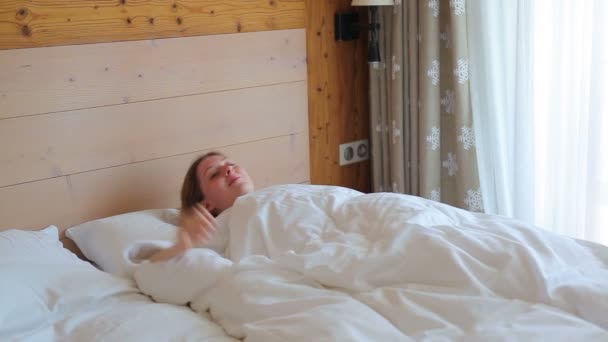 junge Frau wacht im Schlafzimmer auf und schaut auf Fenster - Filmmaterial, Video