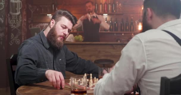 Twee stijlvolle hipster mannen spelen een schaakspel in een bar - Video