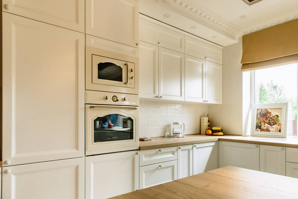 Cucina bianca a parete con forno a microonde e forno. Grande finestra sulla parete destra
. - Foto, immagini