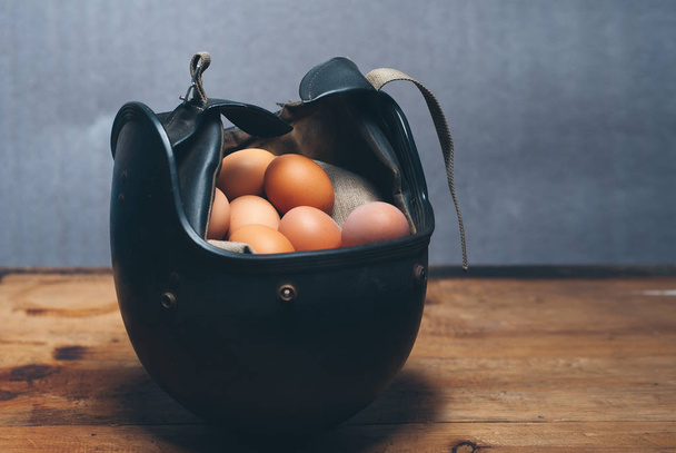 čerstvé kuřecí vejce v ochrannou přilbu, pojem pojištění, vintage černý klobouk jako symbol ochrany - Fotografie, Obrázek