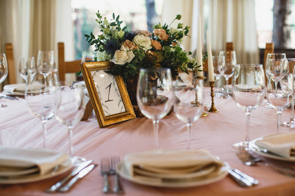 A lots of cutlery and some wineglasses are standing on the table. There is a flower bouquet at the middle of the table. - Foto, immagini