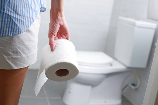 Frau hält Toilettenpapierrolle vor Toilettenschüssel. - Foto, Bild