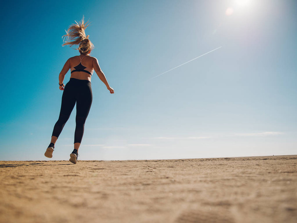 назад вид молодой спортсменки, прыгающей на пляже с солнечным светом
 - Фото, изображение