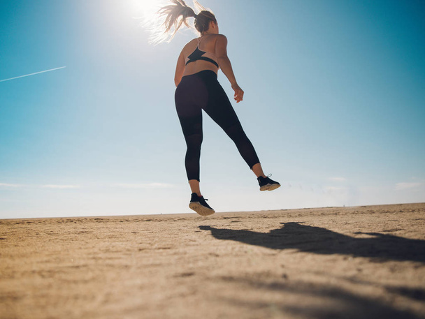 rear view of young sportswoman jumping on sandy beach  - Foto, imagen