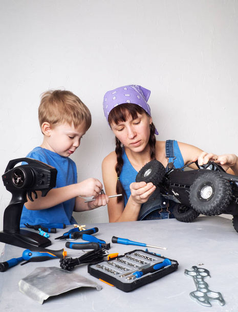 Women in the mens work: Mom helps her son with fixing a radio-controlled buggy model. - Foto, imagen