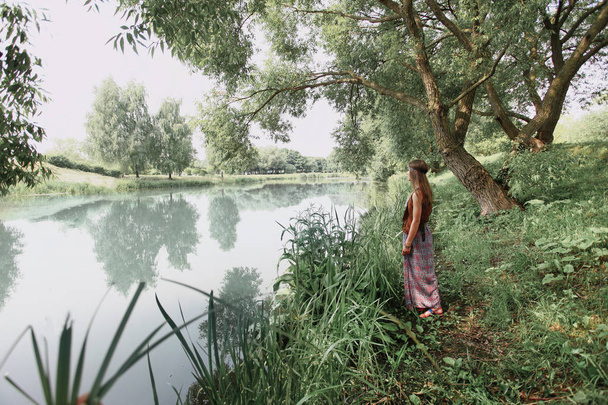 junge Hippie-Frau steht auf dem Gras am See. - Foto, Bild