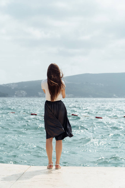 Young woman wear skirt use smartphone takingphotos of sea and mountains at stone pier. Summer vacation at european country. Girl travel on holiday. Woman enjoy and relax life. Summer vibes. - Фото, зображення