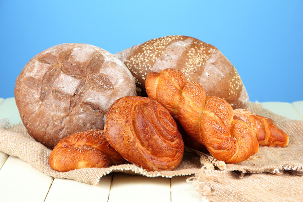 samenstelling met brood, broodjes op rouwgewaad, op houten tafel, op een achtergrond met kleur - Foto, afbeelding
