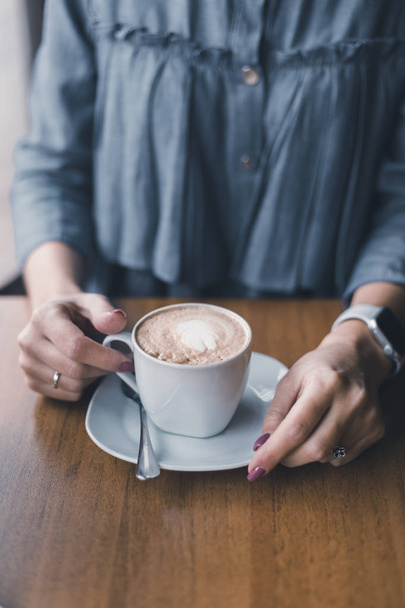 ένα φλιτζάνι του καφέ στα χέρια των γυναικών καπουτσίνο - Φωτογραφία, εικόνα