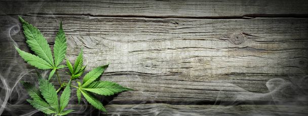 Φύλλα Sativa κάνναβης με καπνό στο ξύλινο τραπέζι - ιατρική μαριχουάνα νομική - Φωτογραφία, εικόνα