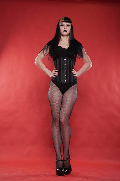 Goth κορίτσι με μαύρα ρούχα σε φόντο κόκκινο στούντιο μόνο - Φωτογραφία, εικόνα