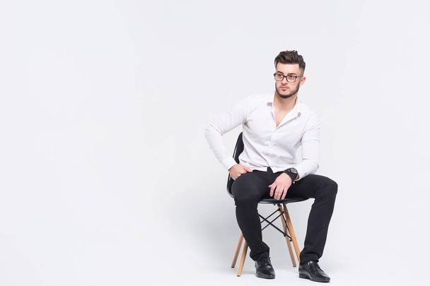 Beautiful brunette man siting at black chair isolated on white background - Fotó, kép
