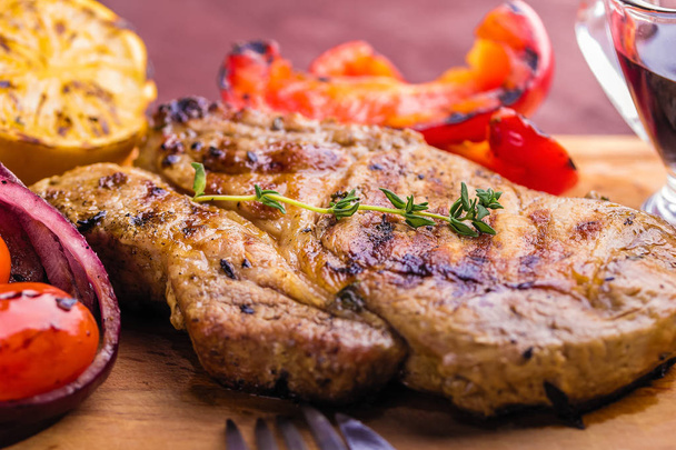 Juicy pork steak with a sprig of fresh thyme, lemon and grilled vegetables close-up - Photo, Image