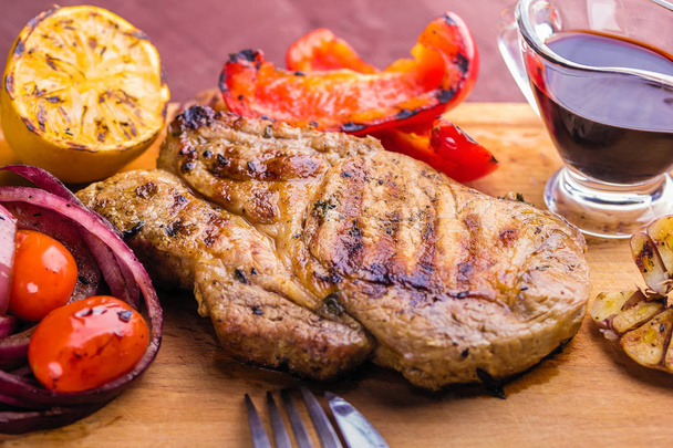 Šťavnatý Vepřový steak s snítka čerstvého tymiánu, citron a grilovanou zeleninou a omáčkou podávané na dřevěném prkénku - Fotografie, Obrázek
