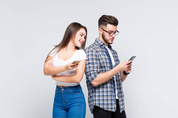 cute woman and handsome man in jeans shirts standing back to back and writing sms on smart phones isolated on white background - Φωτογραφία, εικόνα