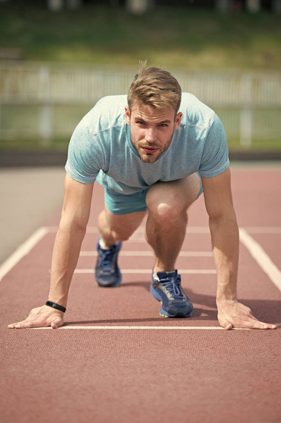 Start of sport career. Man runner on start position stadium background. Sportsman run outdoor at running track. Runner start position running surface. Sportsman on concentrated face ready to go - Фото, изображение